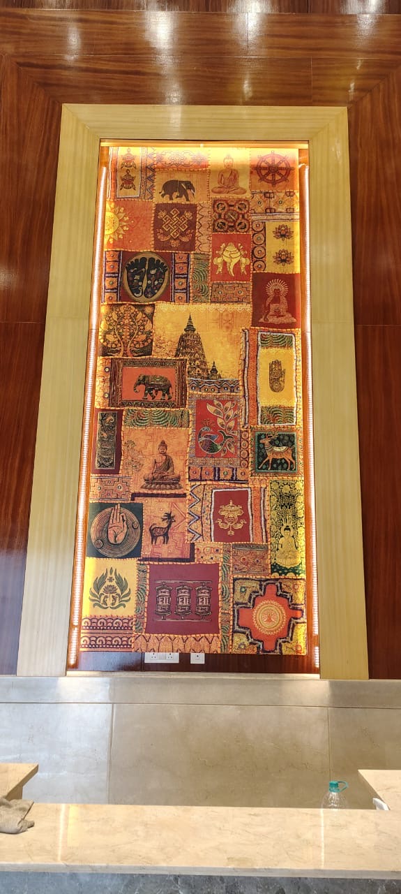 A backlit vertical patchwork tapestry of Indian and Buddhist motifs set in a wood-framed niche — The Artemist, hospitality